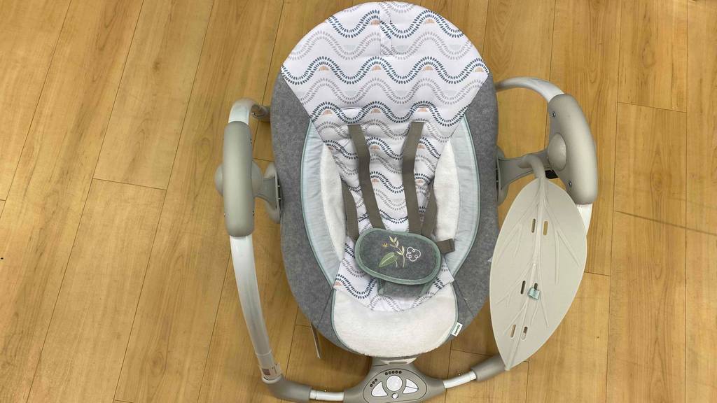 Gesamtansicht von oben einer weiß-grauen, getesteten elektrischen Babywippe, die auf einem Holzboden steht.