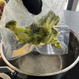 Mit einer Zange wird vakuumierter Brokkoli aus einem Kochtopf entfernt.