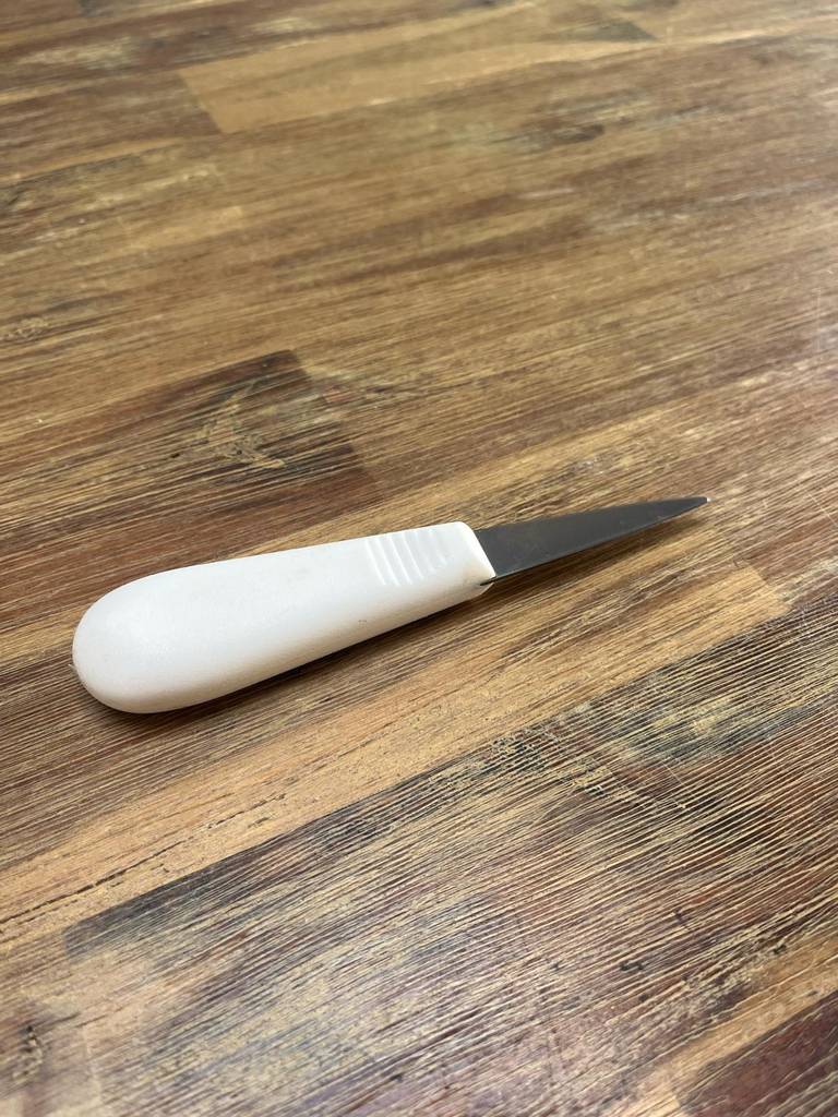 Ein Austernmesser liegt auf einer Holzoberfläche.