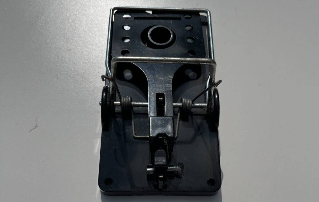 Eine schwarze Rattenfalle im Test inklusive ruhendem Klicksystem auf weißem Untergrund, von oben betrachtet.