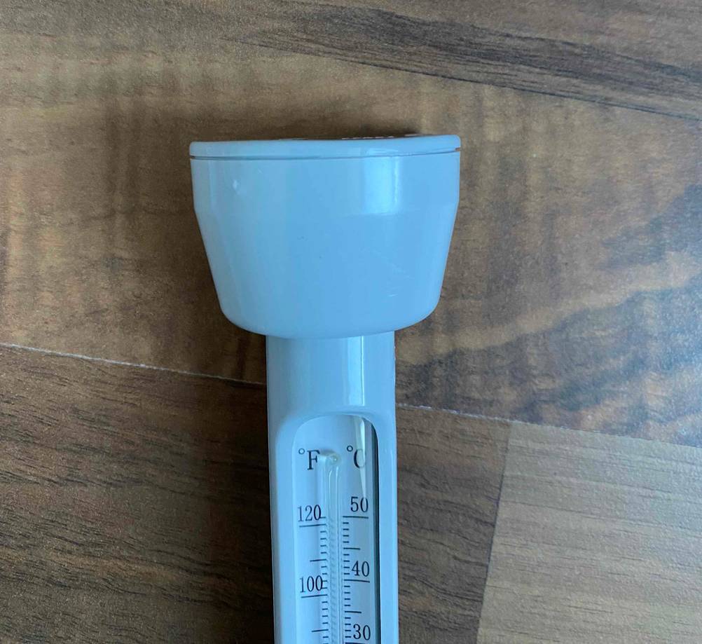 Weißes, analoges Poolthermometer im Test liegt mit Fokus auf den Schwimmer auf einem Holzuntergrund.