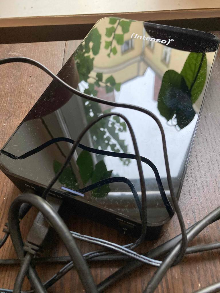 Externe 8-TB-Festplatte in Glänzend-Schwarz liegt mit mehreren Kabeln auf einer Holzoberfläche.