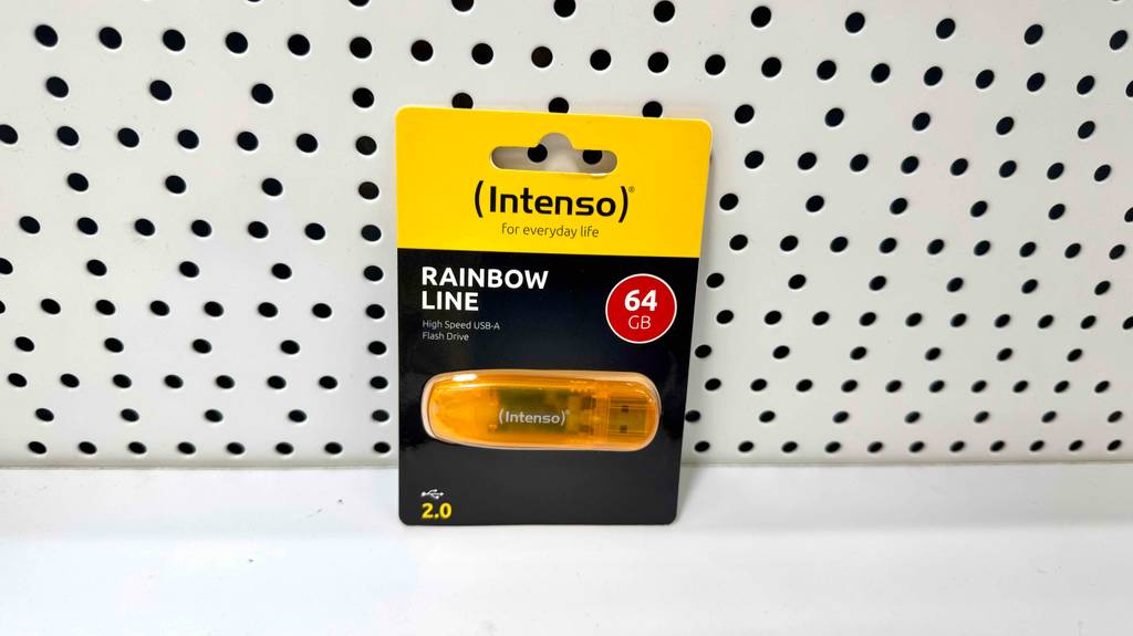 Eine Verpackung mit einem getesteten Intenso USB-Stick lehnt an einer weißen Lochwand.
