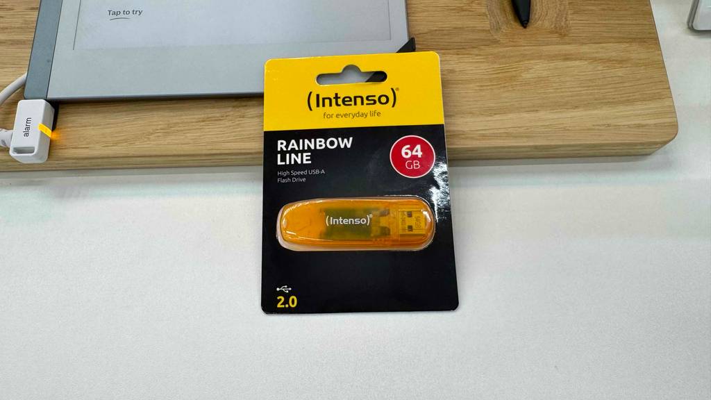 Ein orangefarbener getesteter USB-Stick von Intenso liegt eingeschweißt in der Verpackung auf einer Ausstellungsfläche.