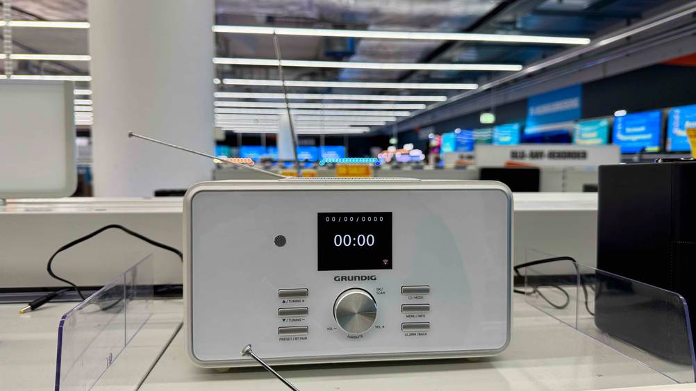 Ein eingeschaltenes Internetradio (weiß) im Test von vorne auf einem Verkaufsregal.