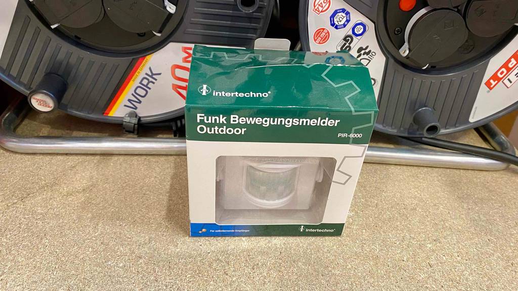 Bewegungsmelder getestet: weiße Verpackung mit grünem Deckel eines Funk-Outdoor-Bewegungsmelders von Intertechno steht vor einem Verkaufsregal mit Kabeltrommeln.