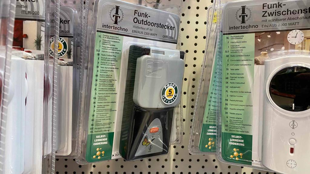 Funksteckdose für außen im Test: Eine transparente Kunststoffverpackung mit einem Funk-Outdoorstecker von Intertechno hängt mit anderen Produkten an einem Verkaufsstand.