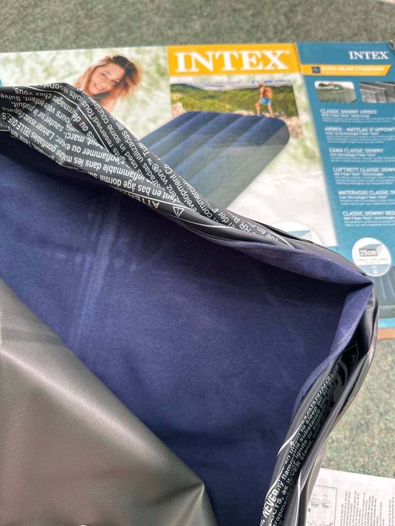 Blaues, getestetes Luftbett der Marke Intex liegt ausgepackt über seiner Originalverpackung.