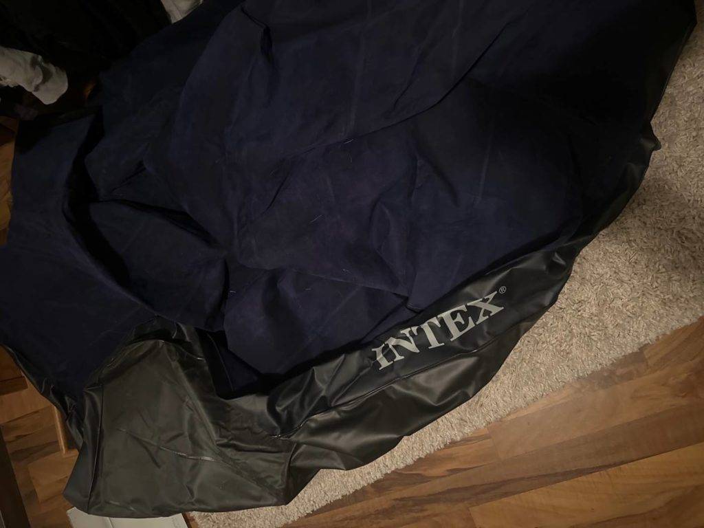 Dunkles, getestetes Luftbett der Marke Intex liegt ohne Luft auf einem hellen Teppichboden