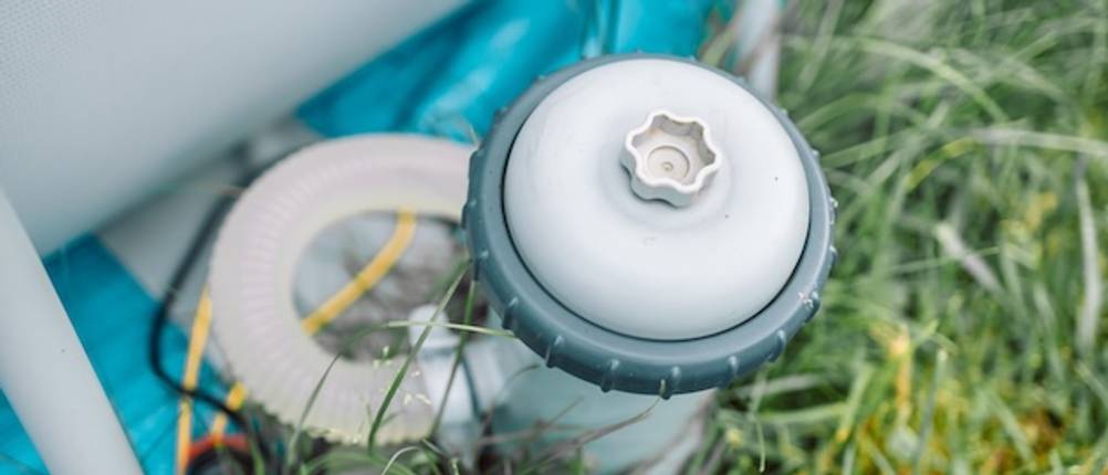Getestete Intex-Filterpumpe im Gras von oben neben einem Pool.