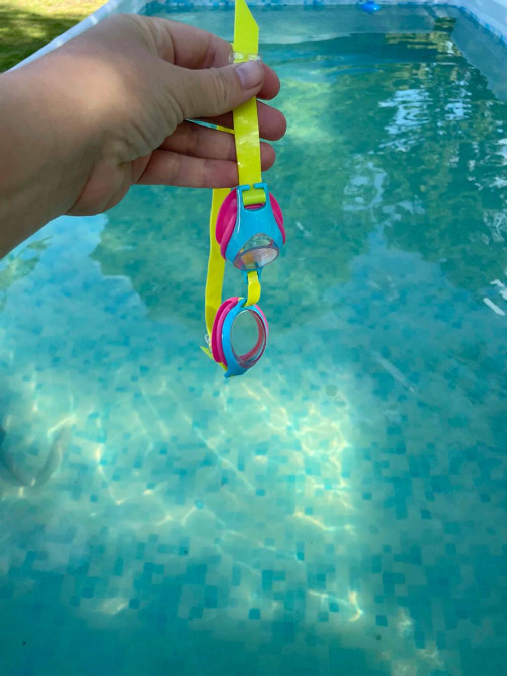 Hand hält eine getestete Schwimmbrille für Kinder über einem Swimmingpool.