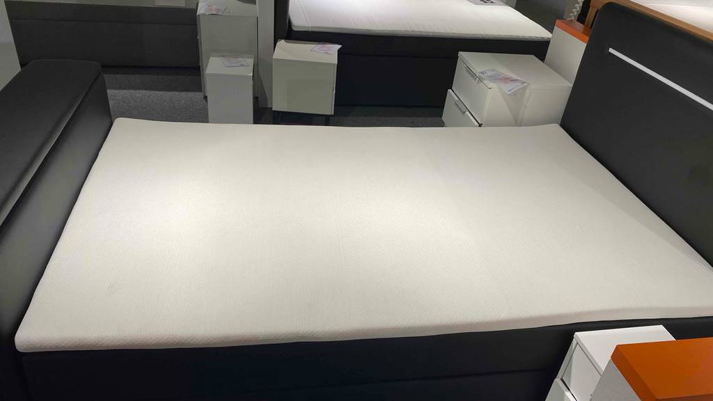 Topper 120x200 im Test: Ein Topper liegt auf einem schwarzen Bett, von der Seite betrachtet.