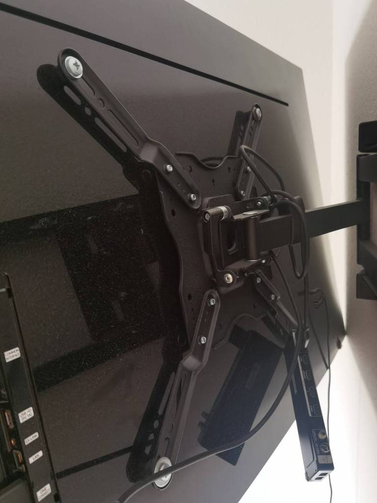 Sicht auf eine auf der Rückseite des Fernsehers montierte, schwarze sowie getestete TV-Wandhalterung.
