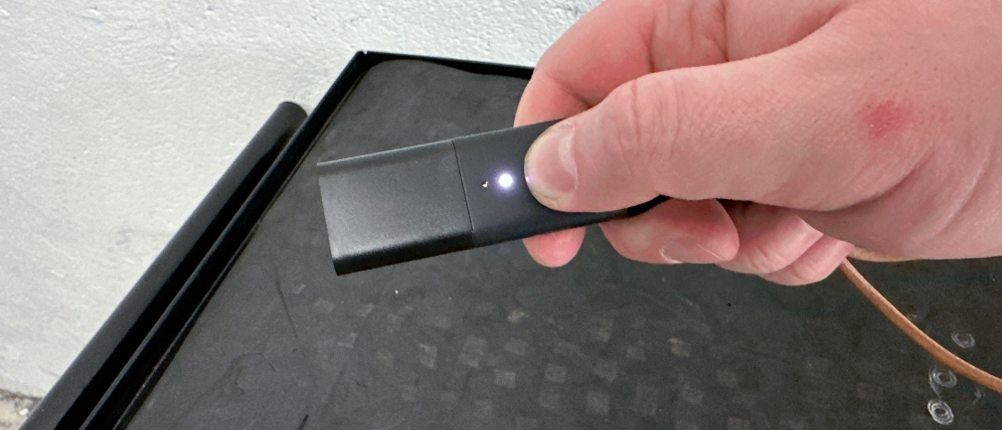 Ein eingeschalteter Invoxia GPS Tracker wird mit der Hand gehalten. Eine kleine LED leuchtet auf der Oberfläche.
