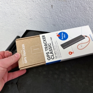 Ein brauner Karton mit Invoxia-Logo wird von einer Hand geöffnet. Das Gerät befindet sich im Inneren in einer Schaumstoffform.