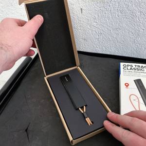 Die geöffnete Verpackung des Invoxia GPS Trackers zeigt das Gerät in einer schwarzen Schaumstoffeinlage. Ein Produktkarton liegt daneben.