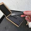 Der Invoxia GPS Tracker wird aus einer geöffneten Verpackung entnommen. Das Gerät ist länglich und hat eine Trageschlaufe.