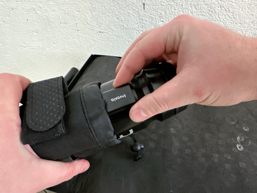 Der Invoxia GPS Tracker wird in eine schwarze Hülle geschoben. Die Hände halten das Gerät während des Einsteckens fest.