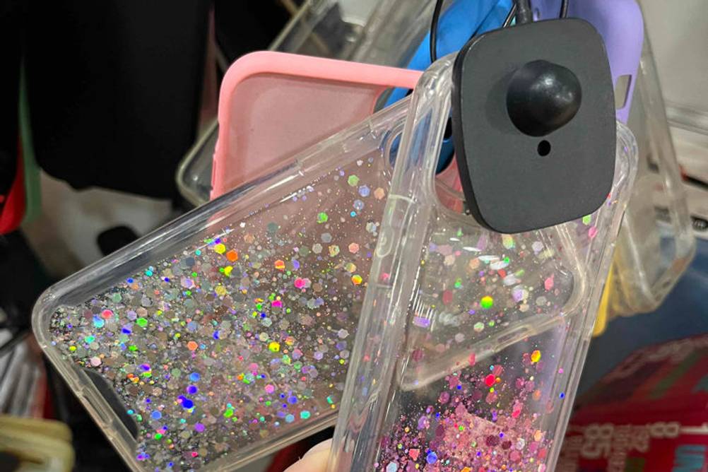 iPhone-12-Mini-Hülle getestet: Mehrere Glitzerhüllen werden am Verkaufsstand von einer Hand berührt.