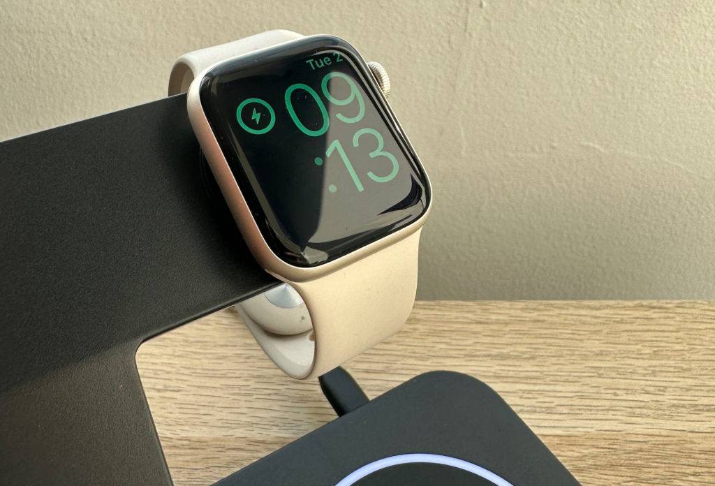 iPhone-Ladestationen-Test: Detailansicht einer schwarzen Ausführung mit eingeschalteter Apple Watch auf der Ladefläche vor einem beigefarbenen Hintergrund.