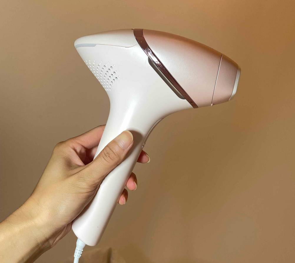 Eine Hand hält ein IPL-Gerät im Test seitlich vor einer hellen Wand.