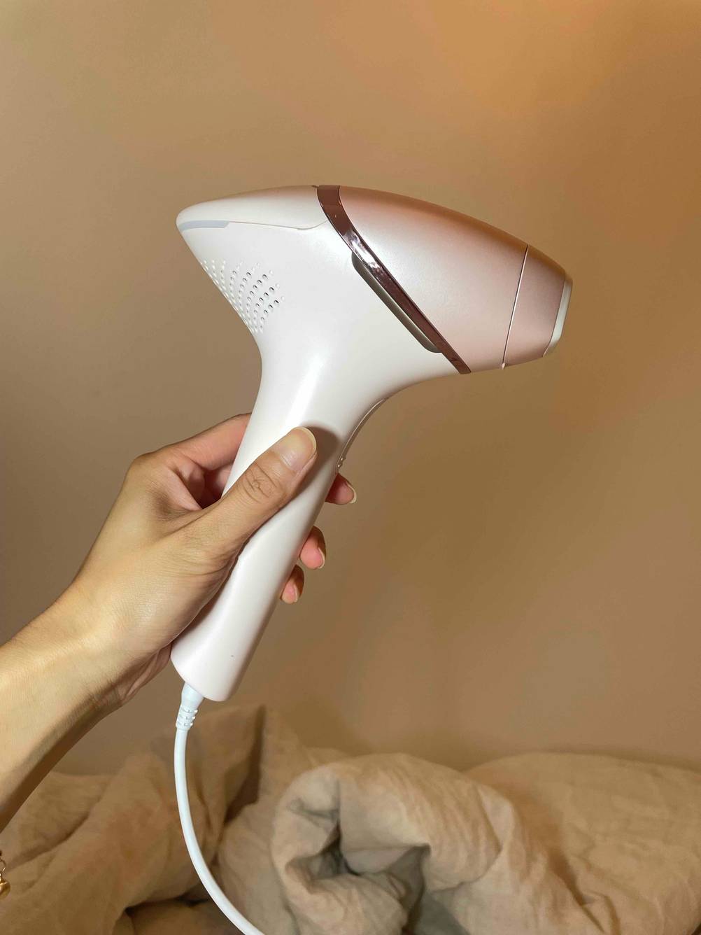 Eine Hand hält ein IPL-Gerät im Test seitlich vor einer hellen Wand.