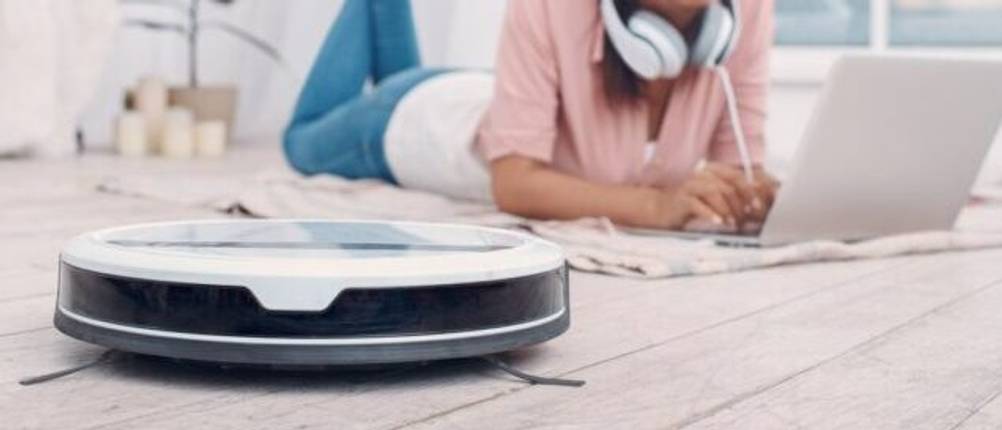 iRobot-Staubsauger-Roboter im Test: Ein Staubsauger-Roboter reinigt einen Boden, während eine Frau daneben auf einer Decke liegt und am Computer arbeitet.