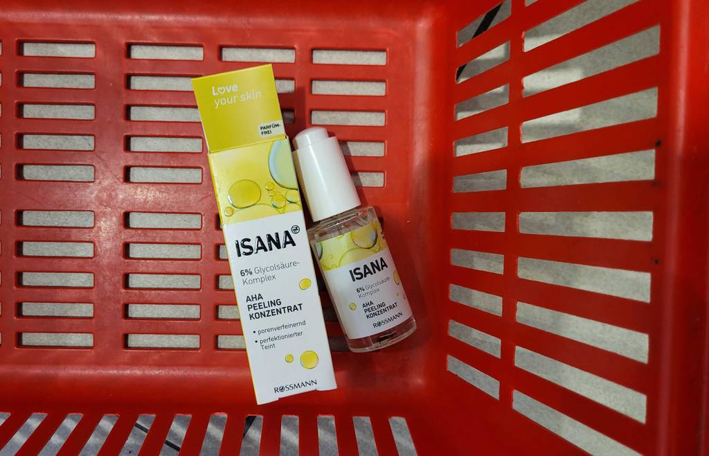 Isana Fruchtsäurepeeling im Test: Nahaufnahme einer weiß-gelben Verpackung neben einem Fläschchen mit AHA Peeling Konzentrat in einem orangen Einkaufskorb.