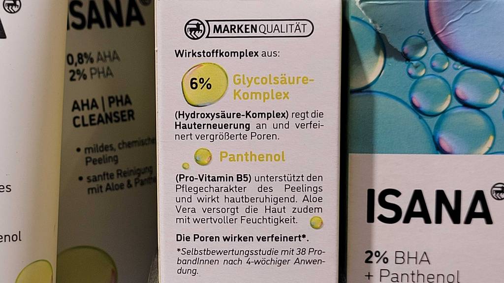 Nahaufnahme der Beschreibung des Wirkstoffkomplexes auf einer weiß-gelben Verpackung mit Isana Fruchtsäurepeeling im Test neben weiteren Isana Produkten.