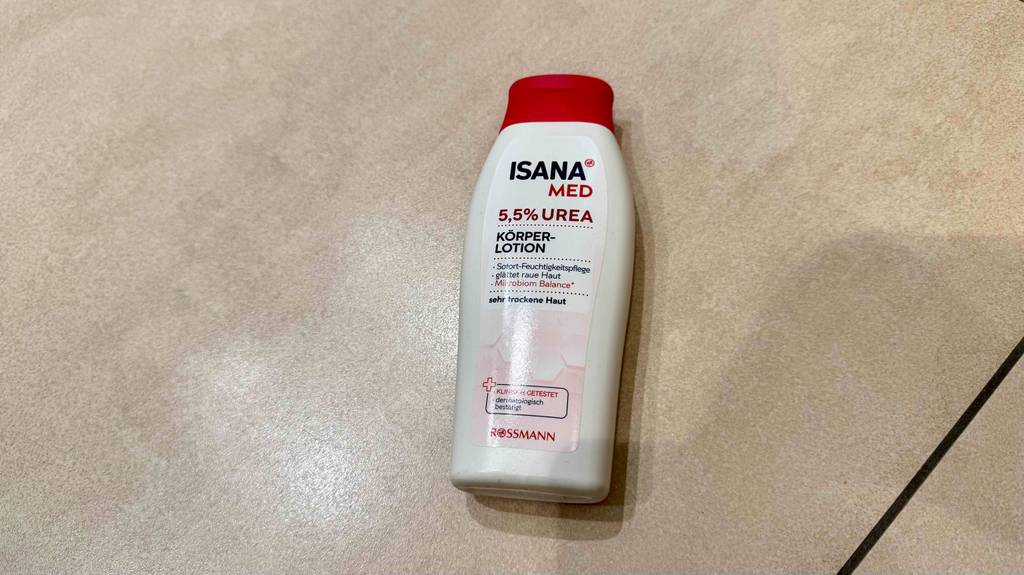 Eine Flasche getestete Bodylotion mit Urea liegt auf einer weißen Fliese.