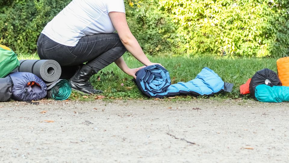 Eine Frau rollt eine Isomatte zusammen, daneben liegen mehrere andere Matten.