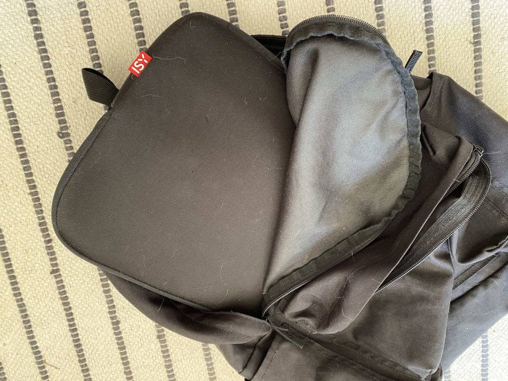 Getestetes Laptop-Sleeve in Schwarz von Isy befindet sich in einem schwarzen Rucksack auf beige-grau gestreiftem Gewebe.