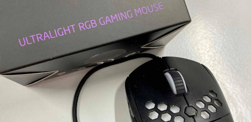 Nahaufnahme des Scrollrads einer Gaming-Maus im Test, die neben ihrer Verpackung mit der Aufschrift: „Ultra light RGB Gaming Mouse“ liegt.