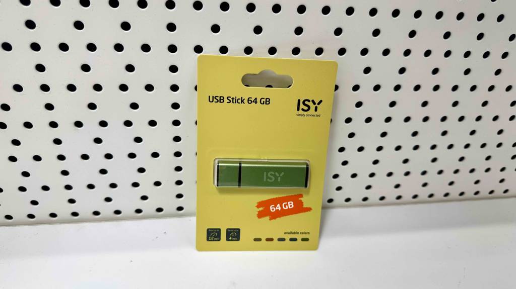 Ein USB-Stick 64 GB im Test lehnt in seiner gelben Verpackung eingeschweißt an einer weißen Lochwand.