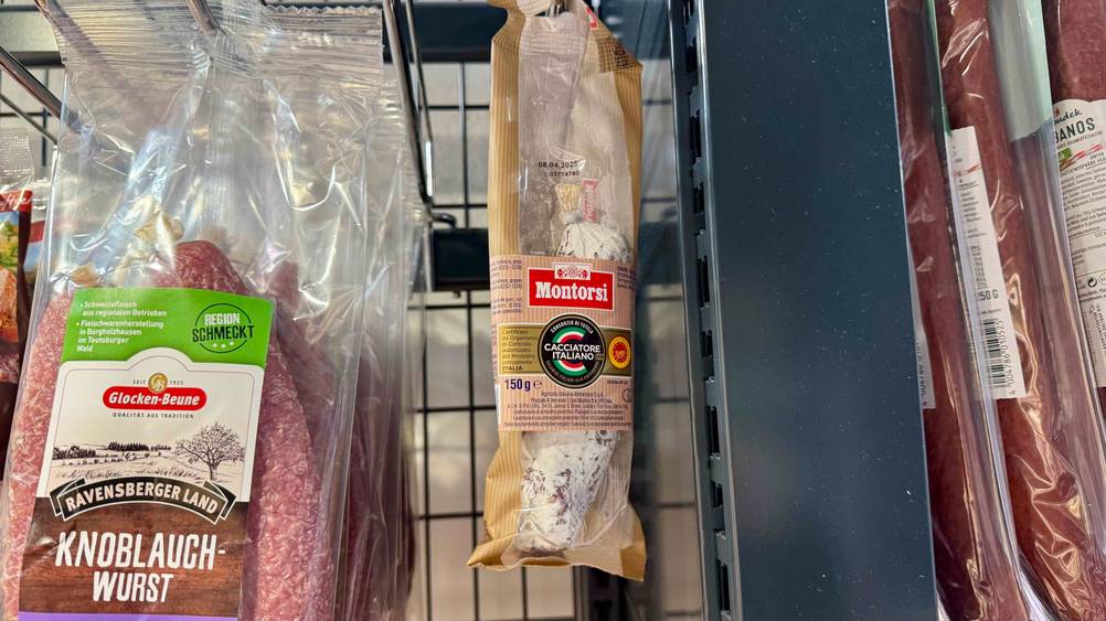 Eine verpackte italienische Salami im Test hängt neben anderen Produkten in einem Verkaufsregal.