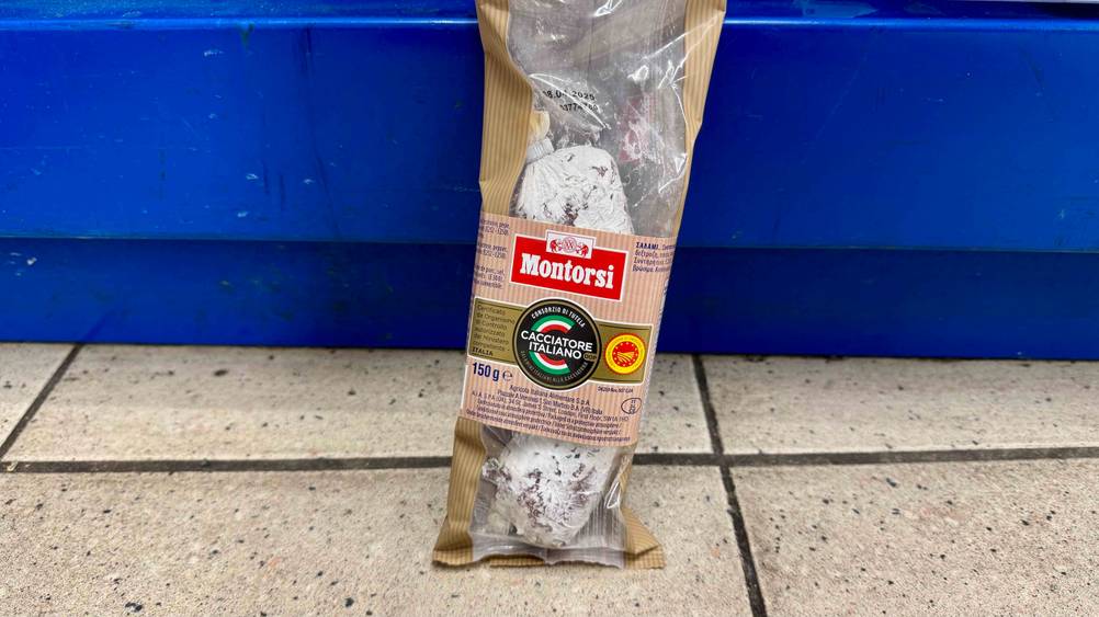 Eine italienische Salami vor einem blauen Regal auf dem Boden stehend.