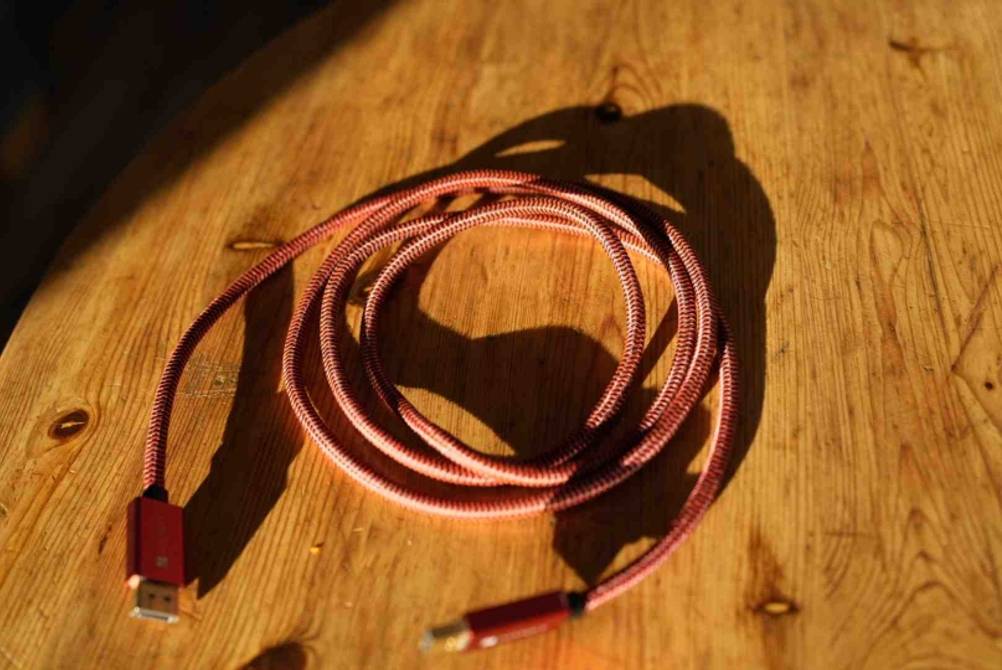 Ansicht von oben auf ein langes, mit rosa Nylon ummanteltes und getestetes DisplayPort-Kabel, das aufgerollt auf einem Holztisch liegt.