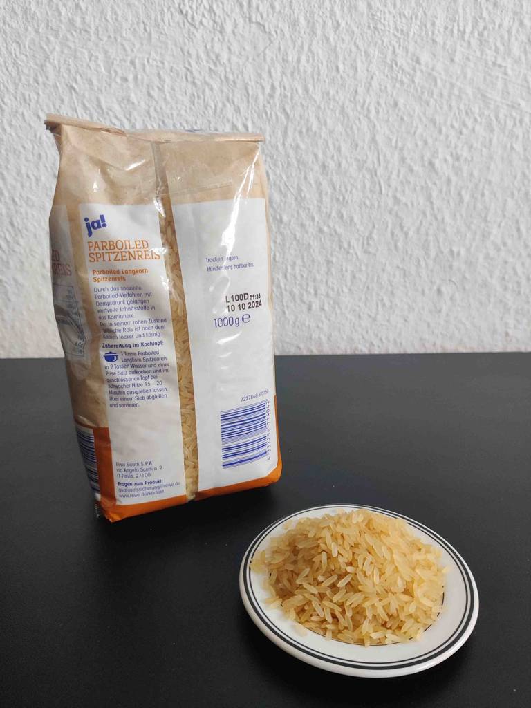 Vor einer 100-g-Packung getesteten Langkornreis steht ein Teller mit ungekochtem Reis.