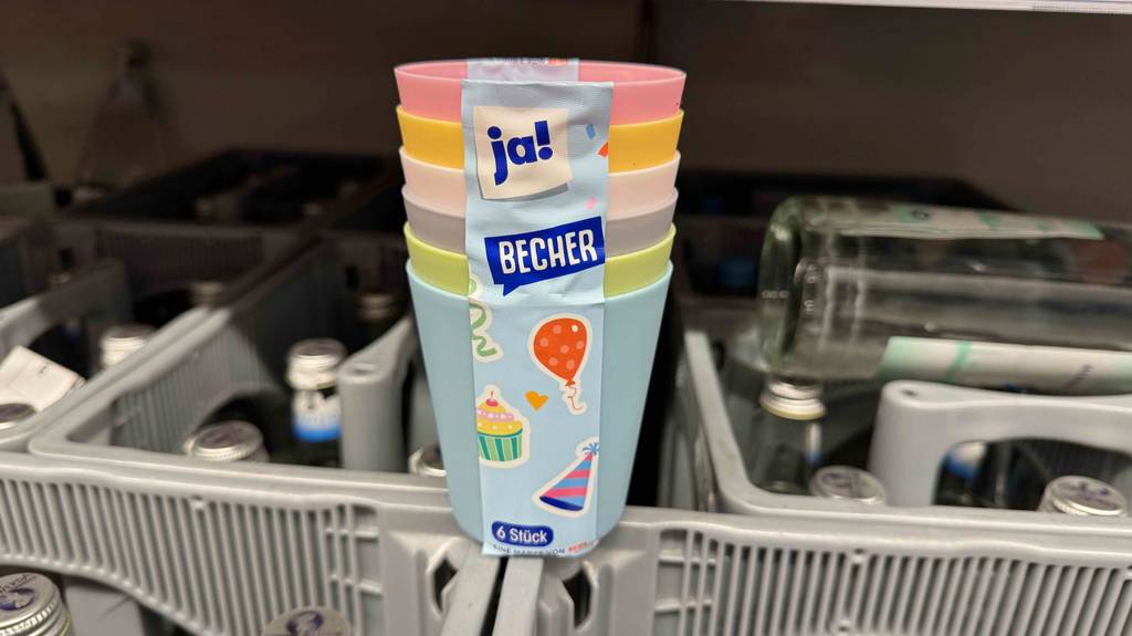 Getestete Plastikbecher in unterschiedlichen Farben stehen ineinandergestapelt auf einem hellgrauen Getränkekasten.