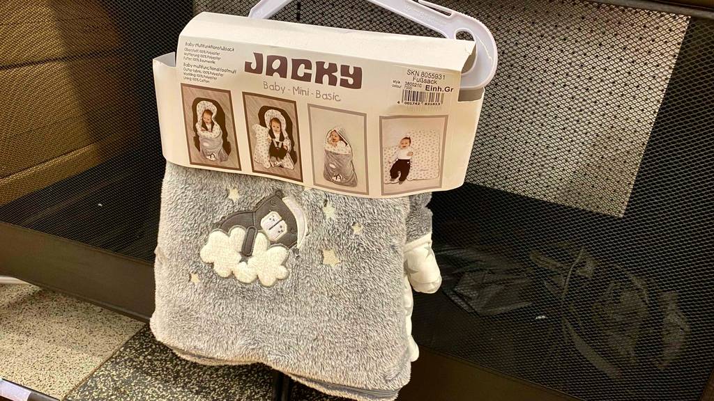 Einschlafdecken-Test: eine graue Jacky Plüschdecke inklusive Fußsack hängt auf einem Bügel an einem Verkaufsstand.