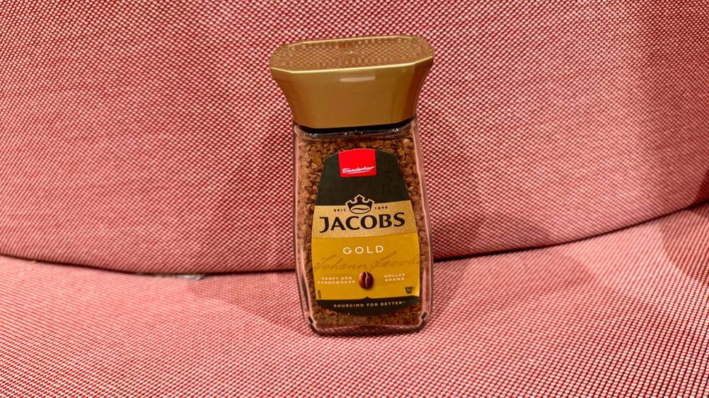 Ein Glas des getesteten Jacobs-Kaffees von schräg oben auf einem roten Polster stehend.