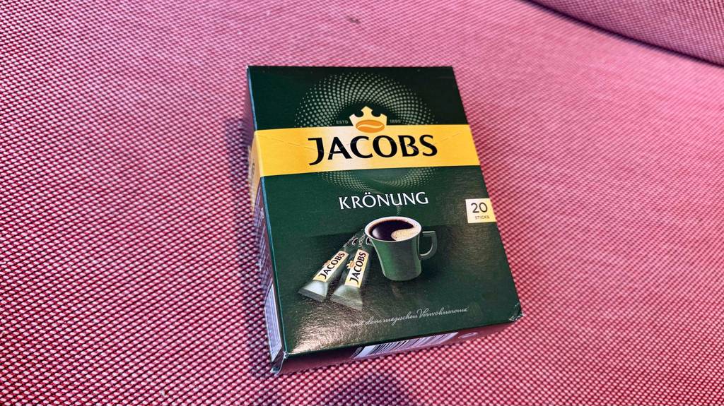 Kaffee-Sticks-Test: Eine grüne Packung Jakobs Krönung inklusive 20 Sticks liegt auf einem roten Sofa.