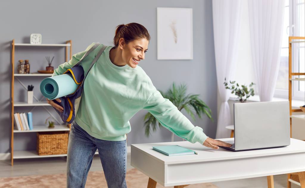 Jade-Yogamatte-Test: Eine Frau trägt eine Yogatasche mit Matte und tippt etwas auf Ihrem Laptop. 