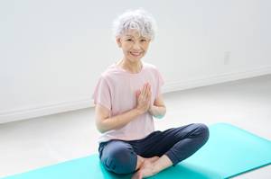 Jade-Yogamatte-Test: Eine ältere Frau sitzt auf einer Yogamatte im Lotussitz. 