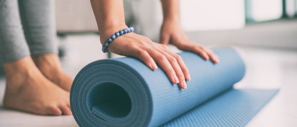 Jade-Yogamatte-Test: Eine Frau rollt eine blaue Yogamatte zusammen. 