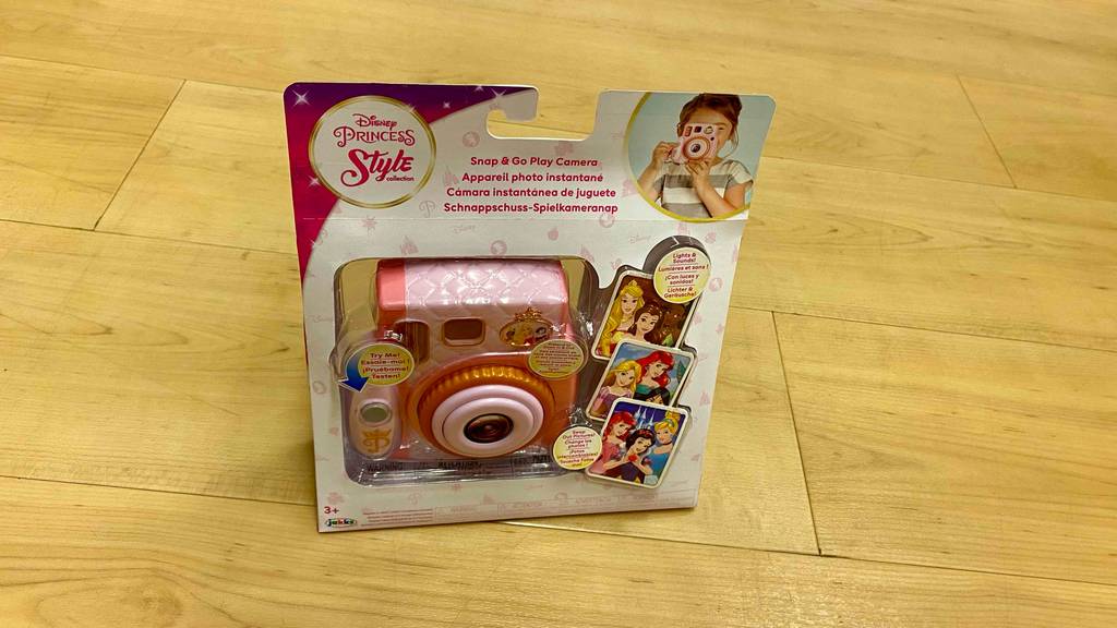 Eine rosa Kinderkamera der Marke Disney Princess steht in seiner Originalverpackung auf einem Parkettboden.
