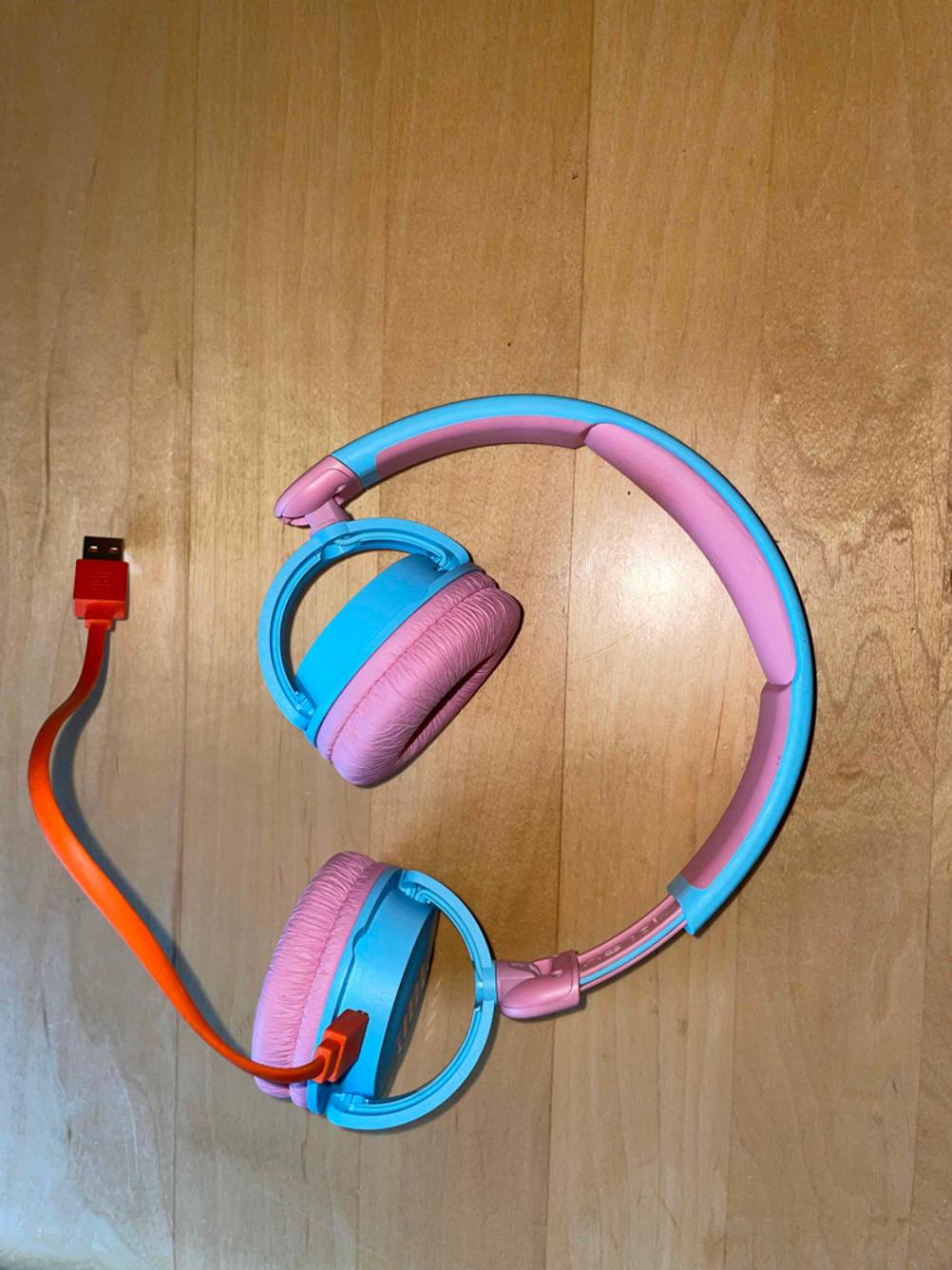 JBL-Kopfhörer mit Ladekabel liegt auf einem Parkettboden