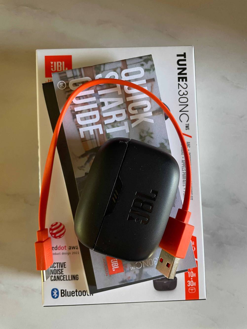 JBL-In-Ear-Kopfhörer getestet: Auf einer Originalverpackung liegt die Bedienungsanleitung und eine Case mit Stromkabel.