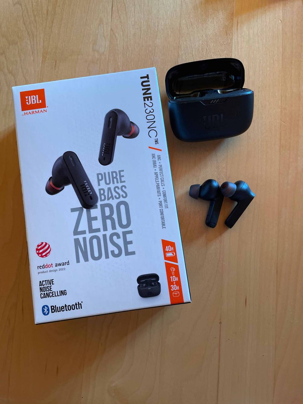 Neben der Originalverpackung liegen die getesteten JBL-In-Ear-Kopfhörer und das Ladecase.