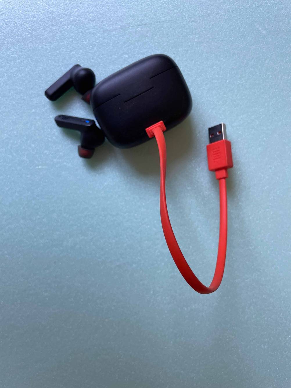 Ein Case mit Stromanschluss, die getesteten JBL-In-Ear-Kopfhörer daneben auf einer blauen Fläche.